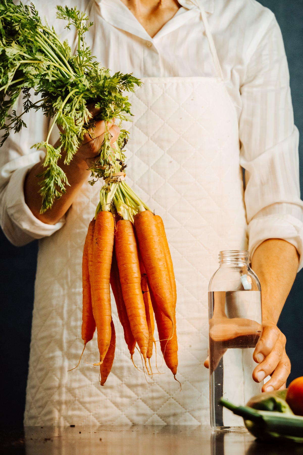person-holds-a-glass-bottle-and-carrots-by-their-tops